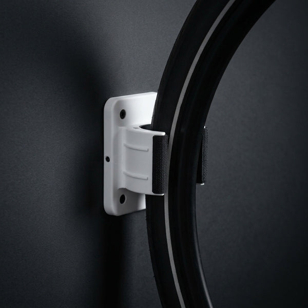 Wall Wheel Clamp in white holding a bike tire against a dark wall, seen from the side