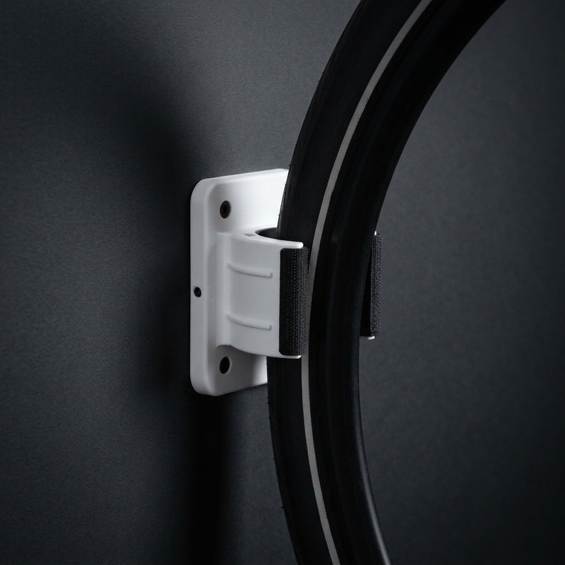 Wall Wheel Clamp in white holding a bike tire against a dark wall, seen from the side