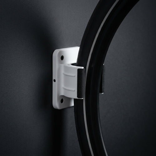 Wall Wheel Clamp in white holding a bike tire against a dark wall, seen from the side